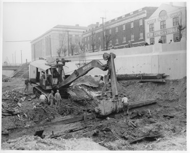 This photograph shows workers carrying out the 1936 federal Works Progress Administration project to fill of the Delaware and Raritan Canal near the State Street Lock No. 7 in the City of Trenton.  The December edition of Highlight, the WPA magazine, praised the elimination of four canal locks and seven bridges related to the “unused and unsightly” canal, which was considered a “community liability” as well as a “health menace in summer months.”  Federal and local officials hailed the filling of the canal and the demolition of its structures, and their replacement by a “fine, modern boulevard.”  The portion of the canal depicted in the photograph is today occupied by the “Trenton Freeway” portion of U.S. Route No. 1.  The tallest building seen in the image was the post office (now the Clarkson S. Fisher Building & U.S. Courthouse), while the brick building was the Trenton Lodge of the Loyal Order of Moose.  Sharp observers will note that the Moose Lodge and adjacent Petry Express & Storage properties are located on site of what is now the New Jersey Department of Environmental Protection building.